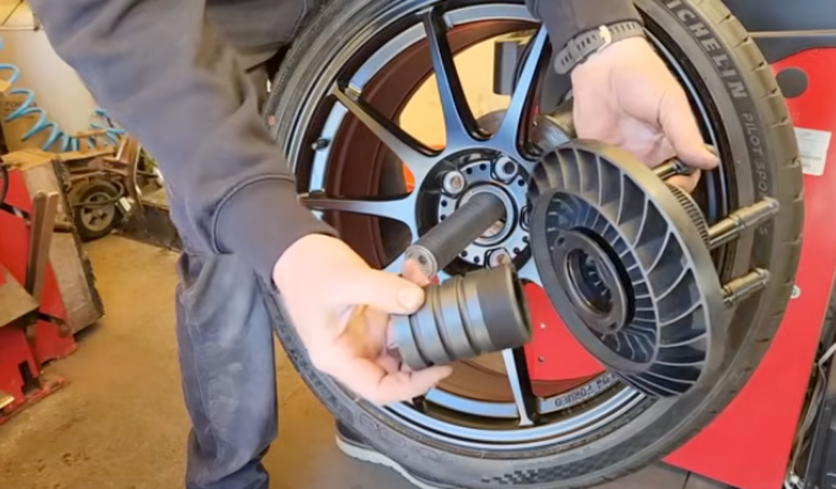 Technician mounting a black alloy wheel on a wheel balancer using a flange plate adapter and centering cone