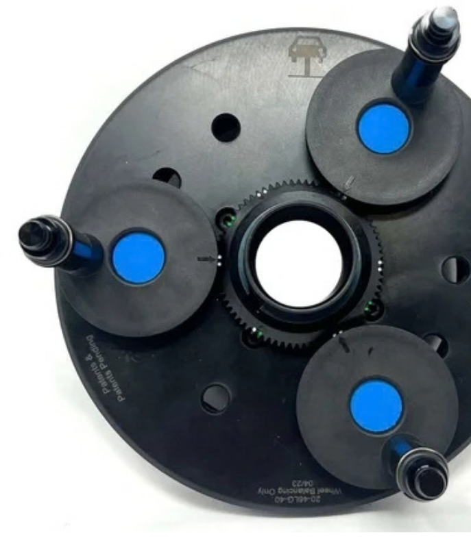 Black wheel balancer flange plate adapter with adjustable mounting pins and a center bore for lug-centric wheel balancing